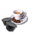 Tazzina di caffè Bacca Rossa con chicchi di caffè tostato sparsi sul piattino. Affianco ci sono due capsule compatibili Dolce Gusto di caffè aromatizzato Cortado.